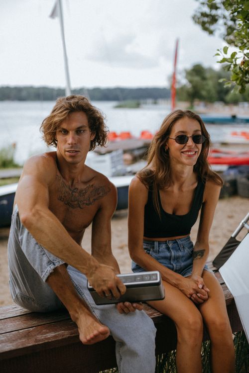 Free Young couple seated on a bench near a scenic lakeside harbor, enjoying a summer day. Stock Photo