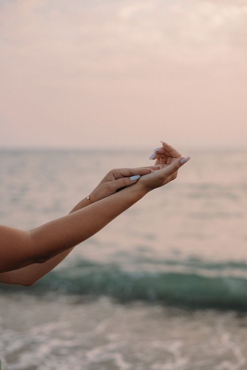 Free Graceful hands with manicured nails extended towards the serene sea at sunset, a perfect blend of elegance and nature. Stock Photo
