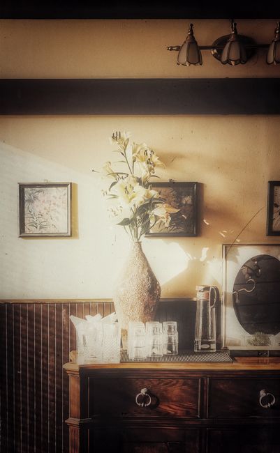 A classic still life of a vintage home interior featuring a vase of flowers and decorative glassware.