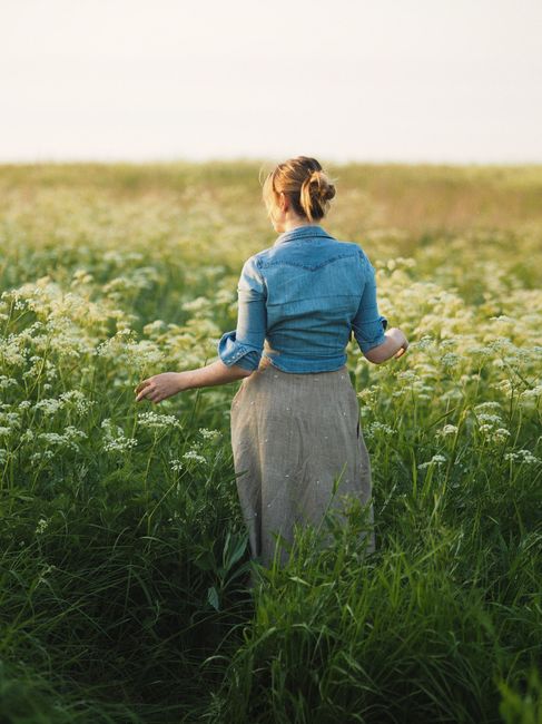 Woman in a denim jacket walking through a lush flower field under the bright daylight.