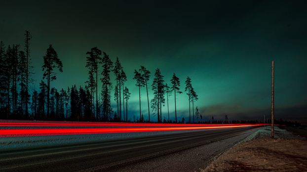 Captivating long exposure of a winter road with red taillight trails under a dark sky.