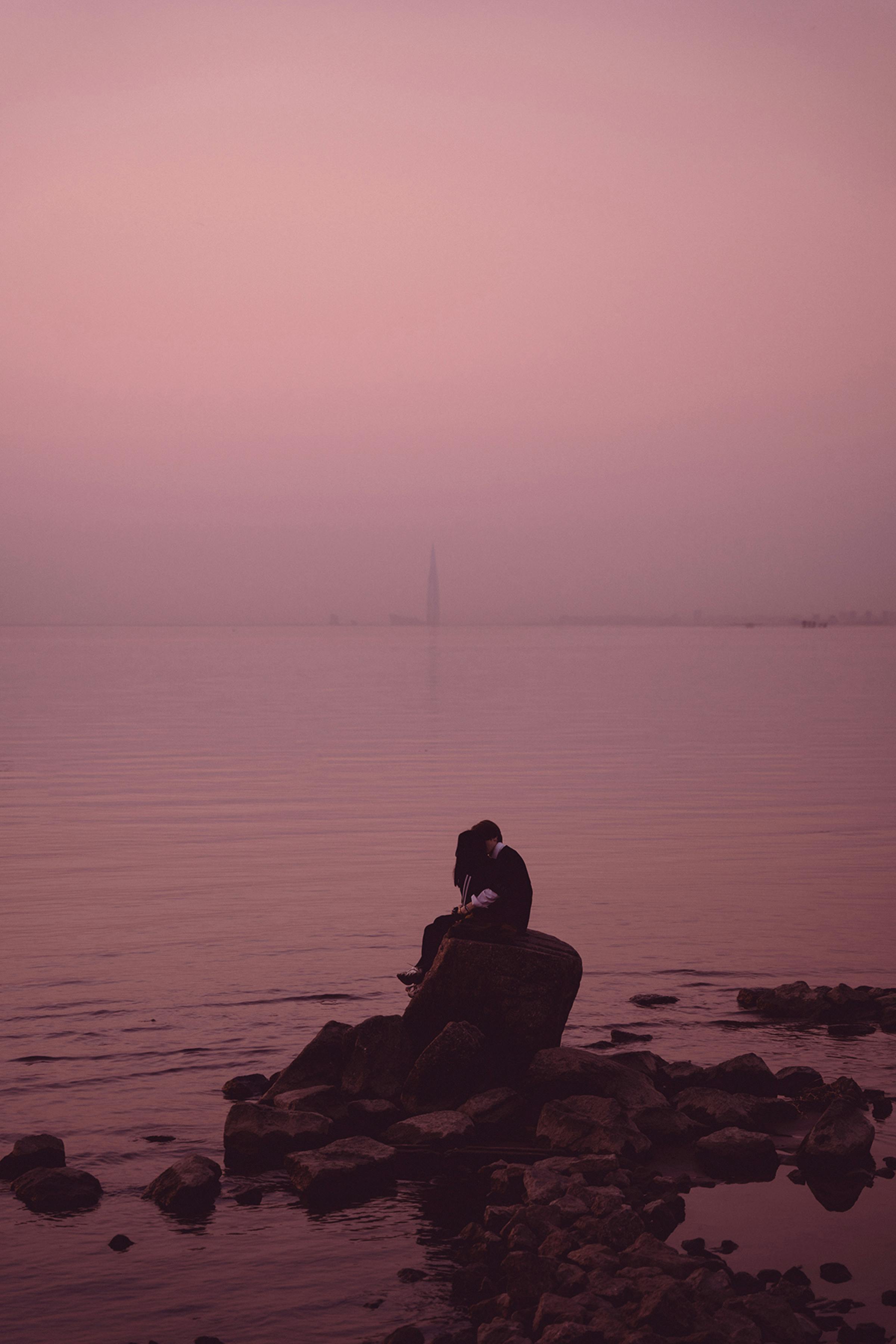 A couple shares a tender moment on rocks by the sea at sunrise in St. Petersburg.