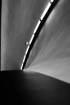 Artistic black and white image of a tunnel with a surveillance camera, showcasing geometric lines and minimalism.