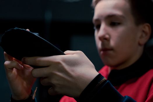 Focused teen boy tapes hockey stick in dimly lit locker room, preparing for game.