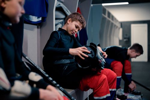 Free Teen ice hockey players in the locker room, getting ready with safety gear. Stock Photo