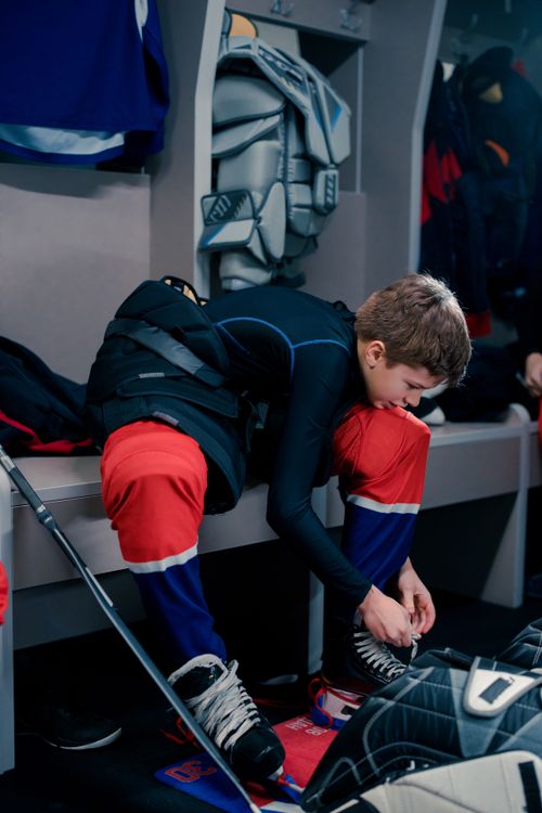 Free Teen hockey player lacing skates in locker room, preparing for game with gear. Stock Photo