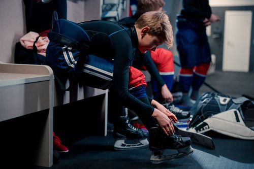Free Teenagers in hockey gear preparing in a locker room, lacing up skates and adjusting protective gear. Stock Photo