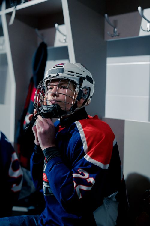 Free Teen hockey player adjusting helmet in locker room before a game, showcasing focus and determination. Stock Photo