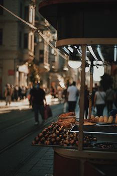 A vibrant street food stall offering grilled corn and chestnuts in a busy urban environment during the day.