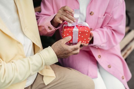 Close-up of a senior couple exchanging a red dotted gift outdoors.