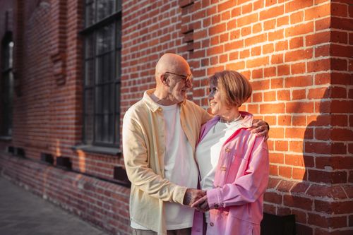Free A senior couple smiling warmly at each other while standing on a sunlit brick street. Stock Photo