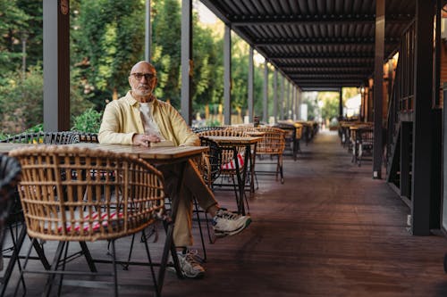 Elderly Man in Yellow Shirt and Eyeglasses Sitting on Wooden Chair on Patio