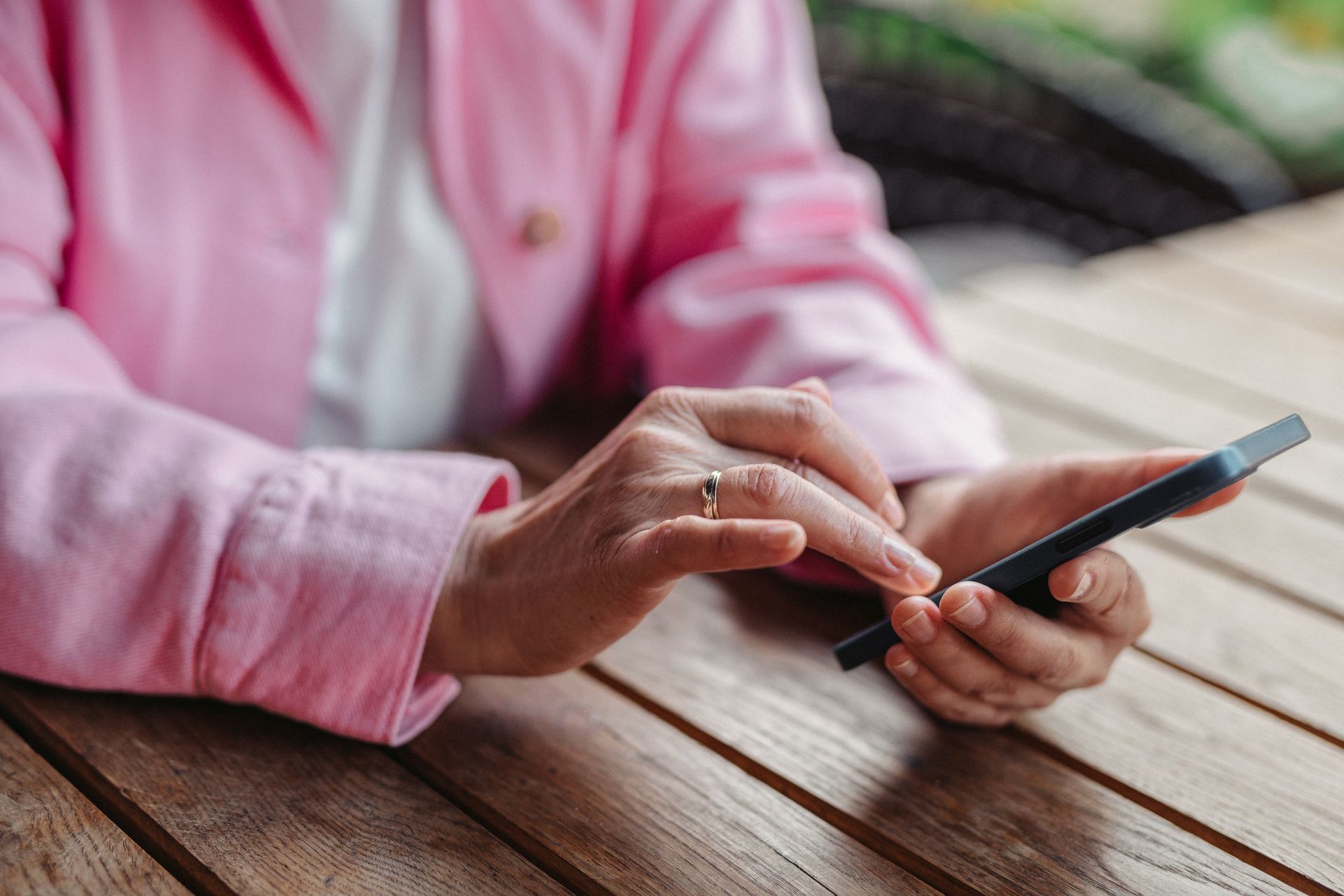A person in pink sleeves texting on a smartphone with a wooden table background.