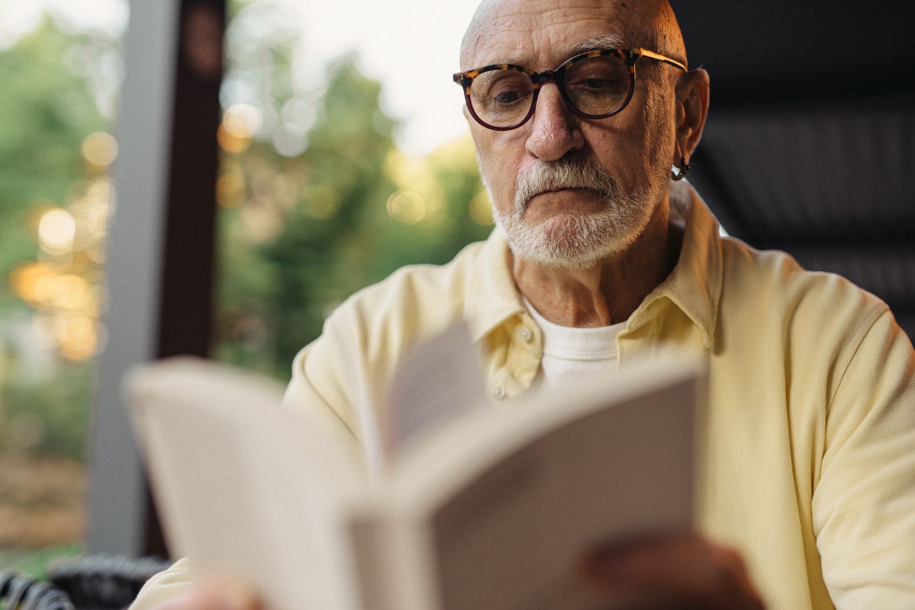 Older man wearing glasses reading a book outdoors