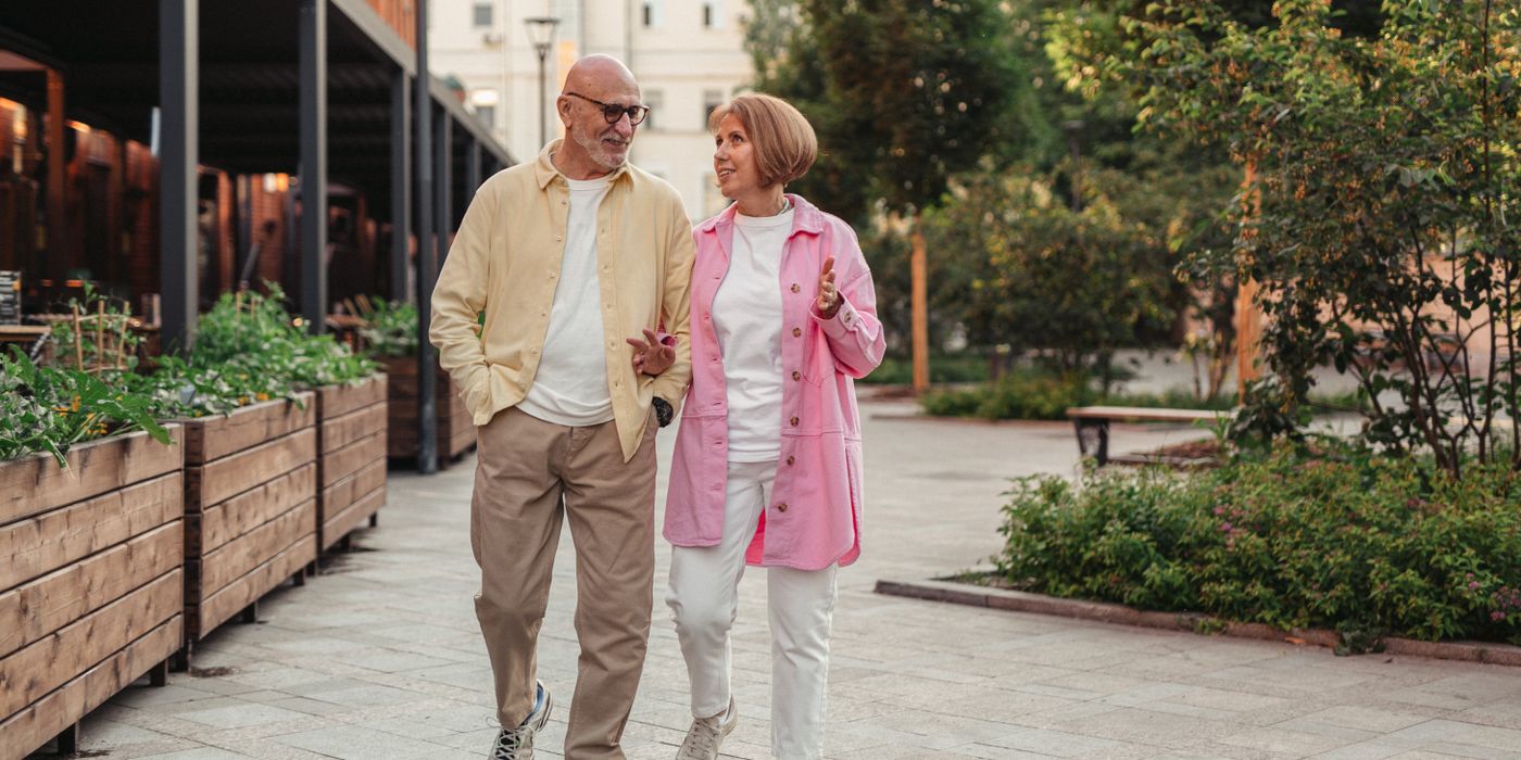 Happy senior couple walking together in a lush outdoor urban setting.