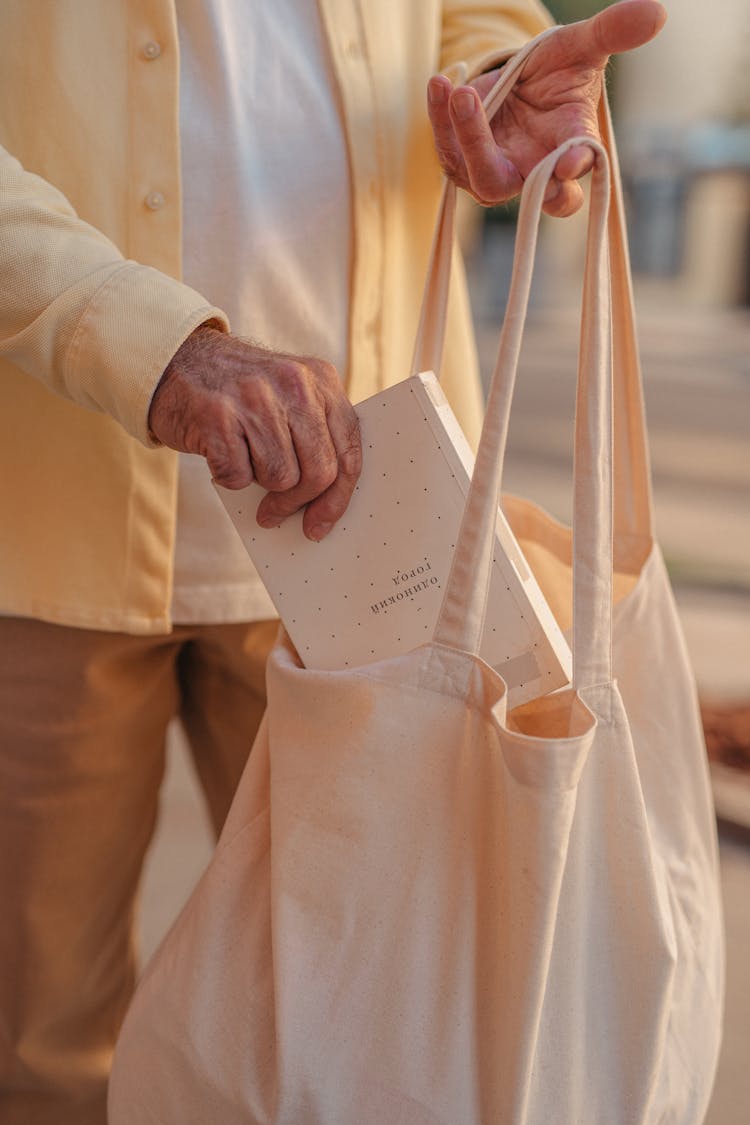 Person Putting A Book In Canvas Tote Bag