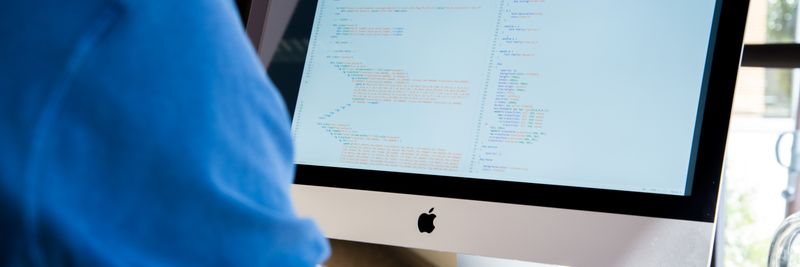 A programmer in a blue shirt coding on an iMac. Perfect for technology or work-related themes.