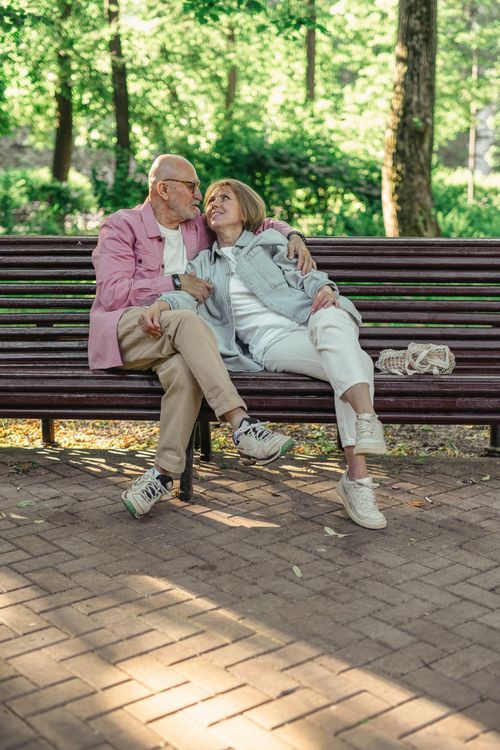Free Elderly couple enjoys a sunny moment on a park bench surrounded by greenery, symbolizing love and companionship. Stock Photo