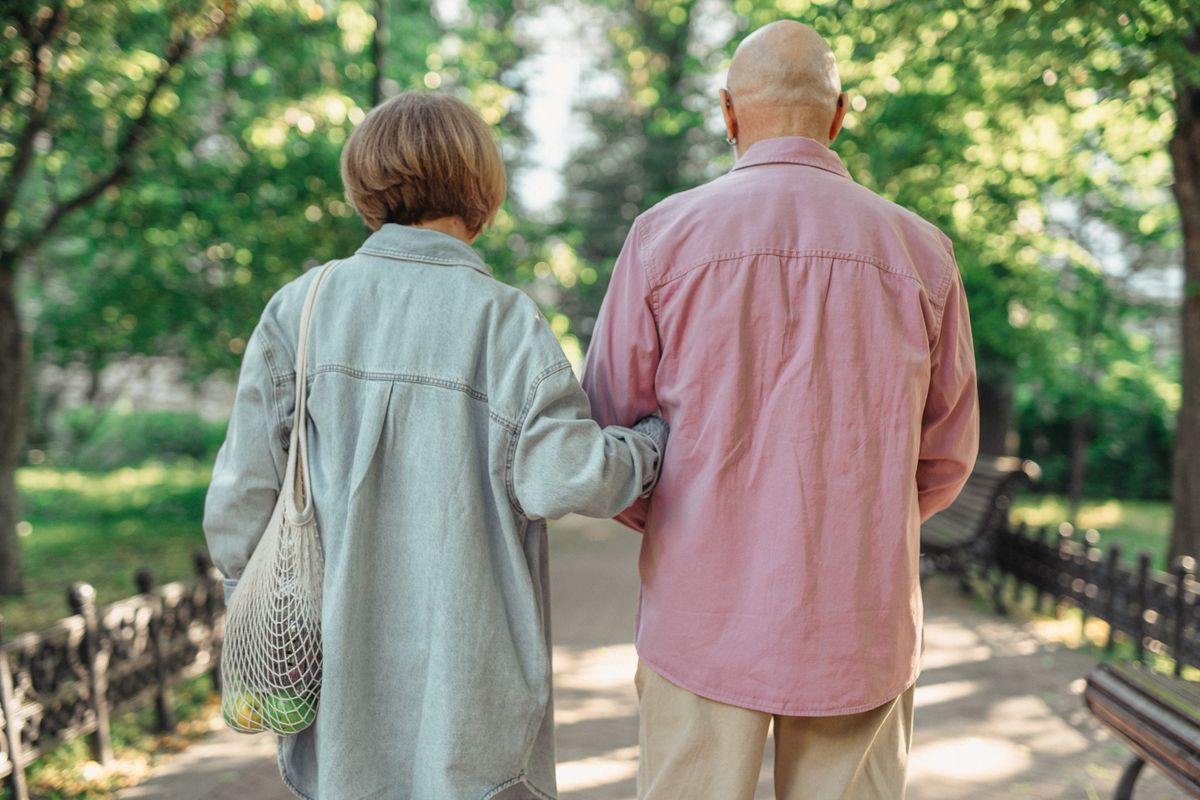 Un couple de seniors marche ensemble dans un parc baigné de soleil