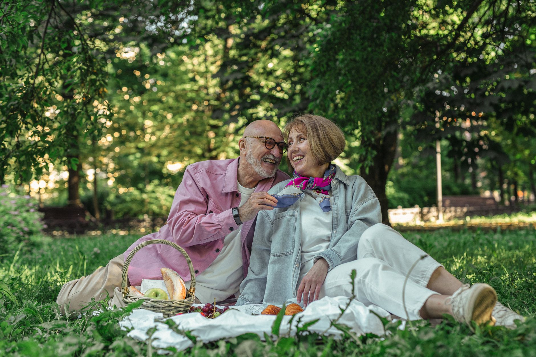 Un couple de seniors sourit et discute ensemble dans un parc après avoir choisi son appareil auditif.