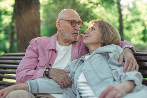Free Senior couple sitting on a wooden bench outdoors, expressing love and togetherness. Stock Photo