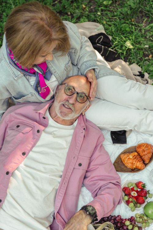 Free Senior couple relaxing outdoors with croissants and fruits, enjoying a picnic together. Stock Photo