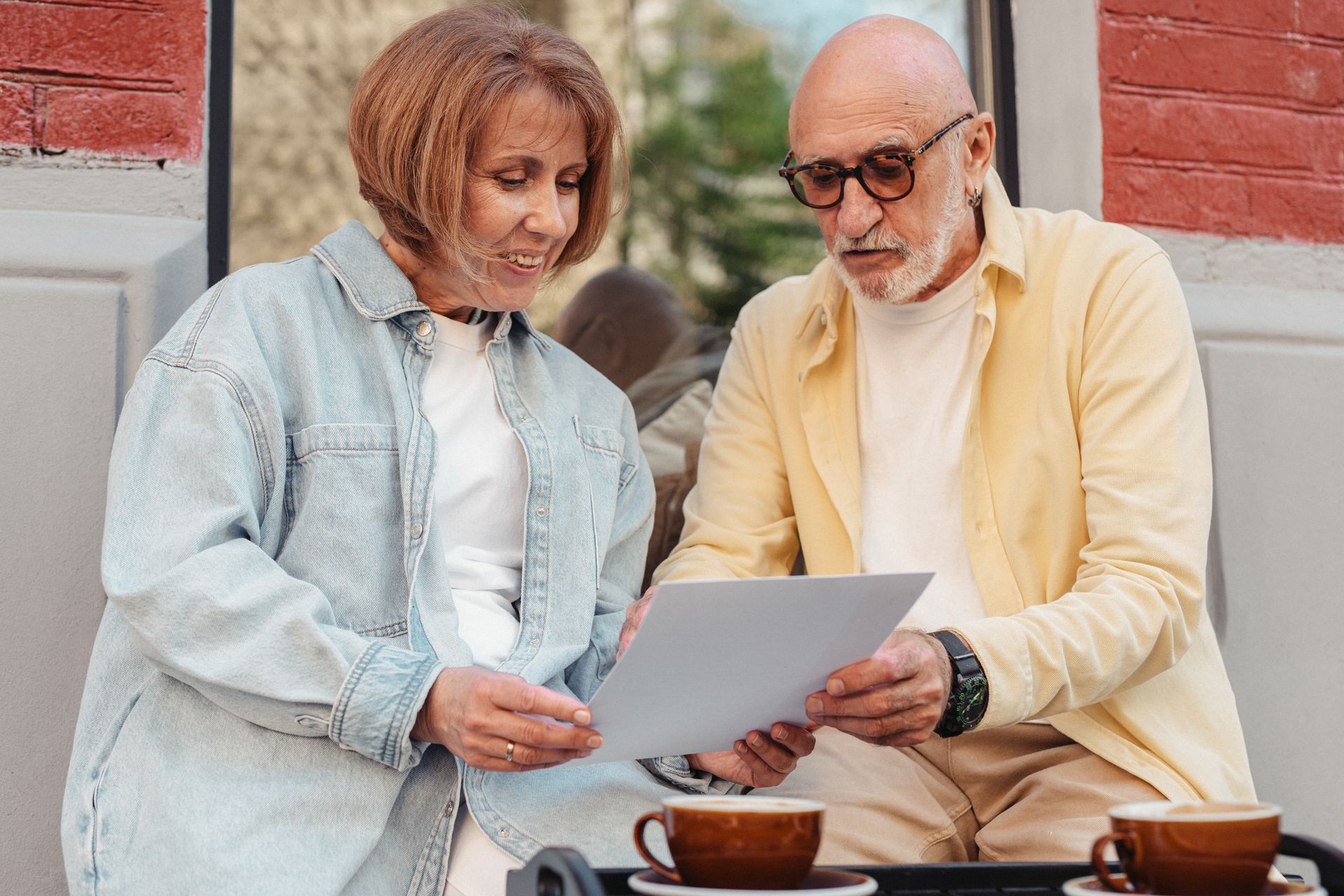 Elderly couple reading a document together while sitting outside at a cafe.