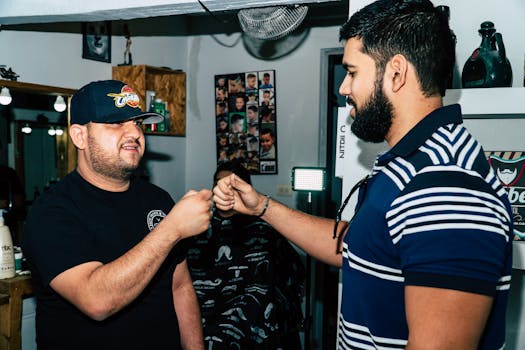 Two men share a friendly fist bump in a stylish, urban barbershop setting.