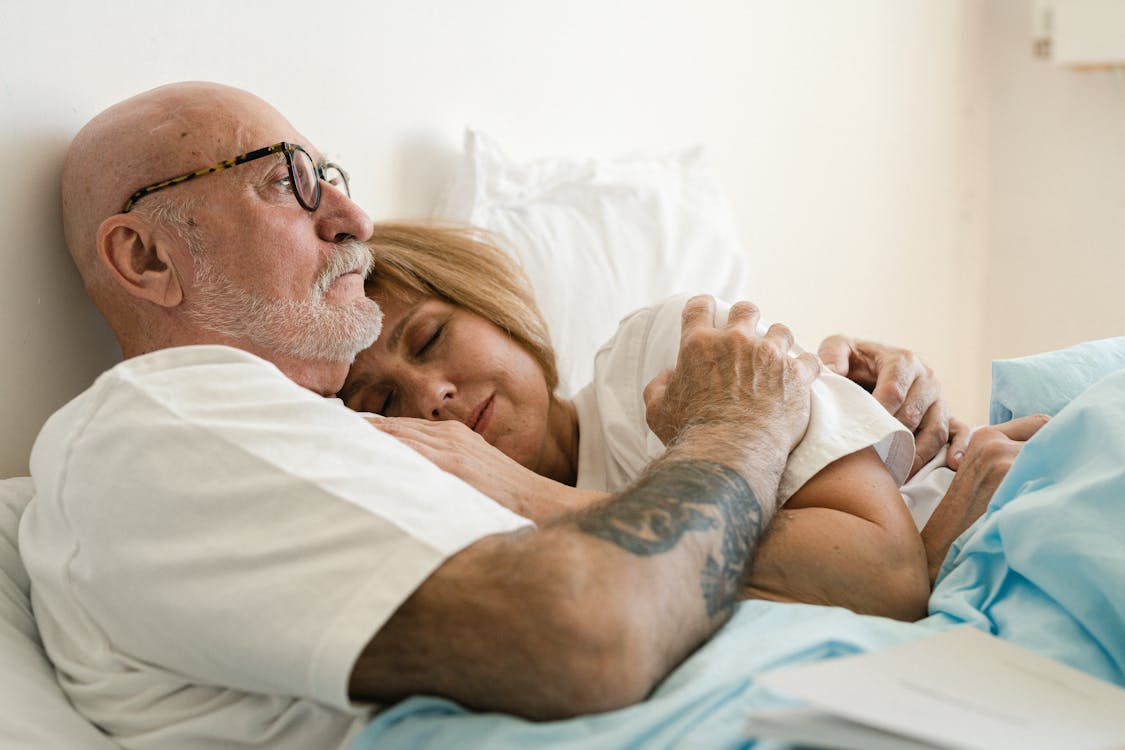 An elderly couple sitting closely on a couch, showing affection.