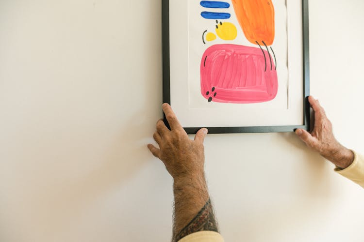 A Tattooed Person Hanging A Framed Art