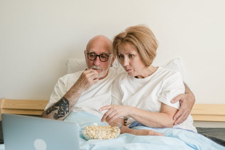 A Couple Eating Popcorn On The Bed