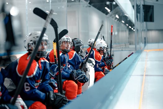 Young hockey players in full gear sit on the bench during an ice hockey game inside an ice rink.