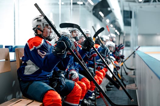 Young ice hockey players in uniforms sitting on the bench during a game, holding hockey sticks.
