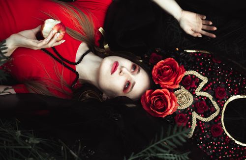 Free A creative and dramatic portrait of a woman in costume holding an apple, adorned with roses and ornate design. Stock Photo