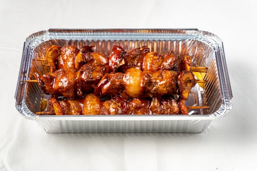 Tasty grilled meat skewers served in a foil tray, perfect for meals.