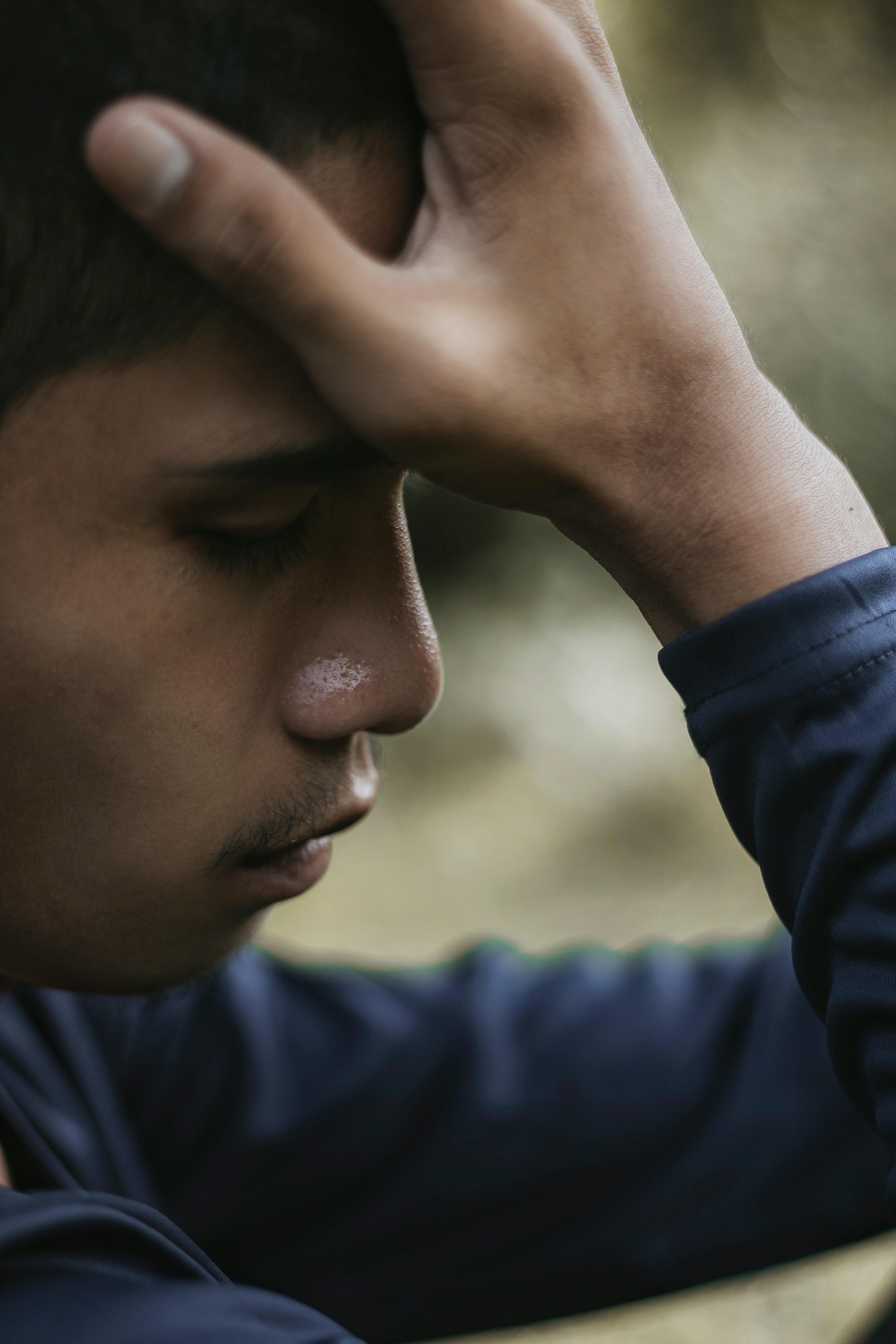 Side view of a young man with eyes closed, hand on forehead, showing emotion.