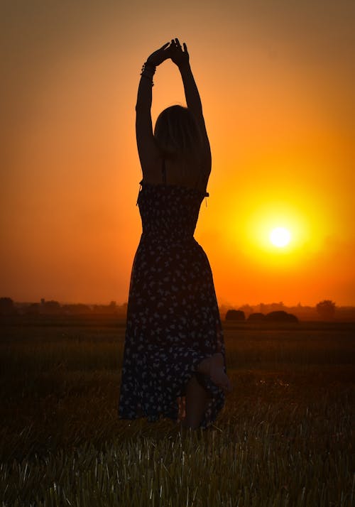 Free Carefree Woman In Long Dress Standing on A Rice Field During Sunset Stock Photo