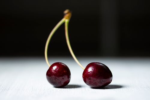 Free Close-up of vibrant, fresh cherries with stems on a white surface with a blurred background. Stock Photo