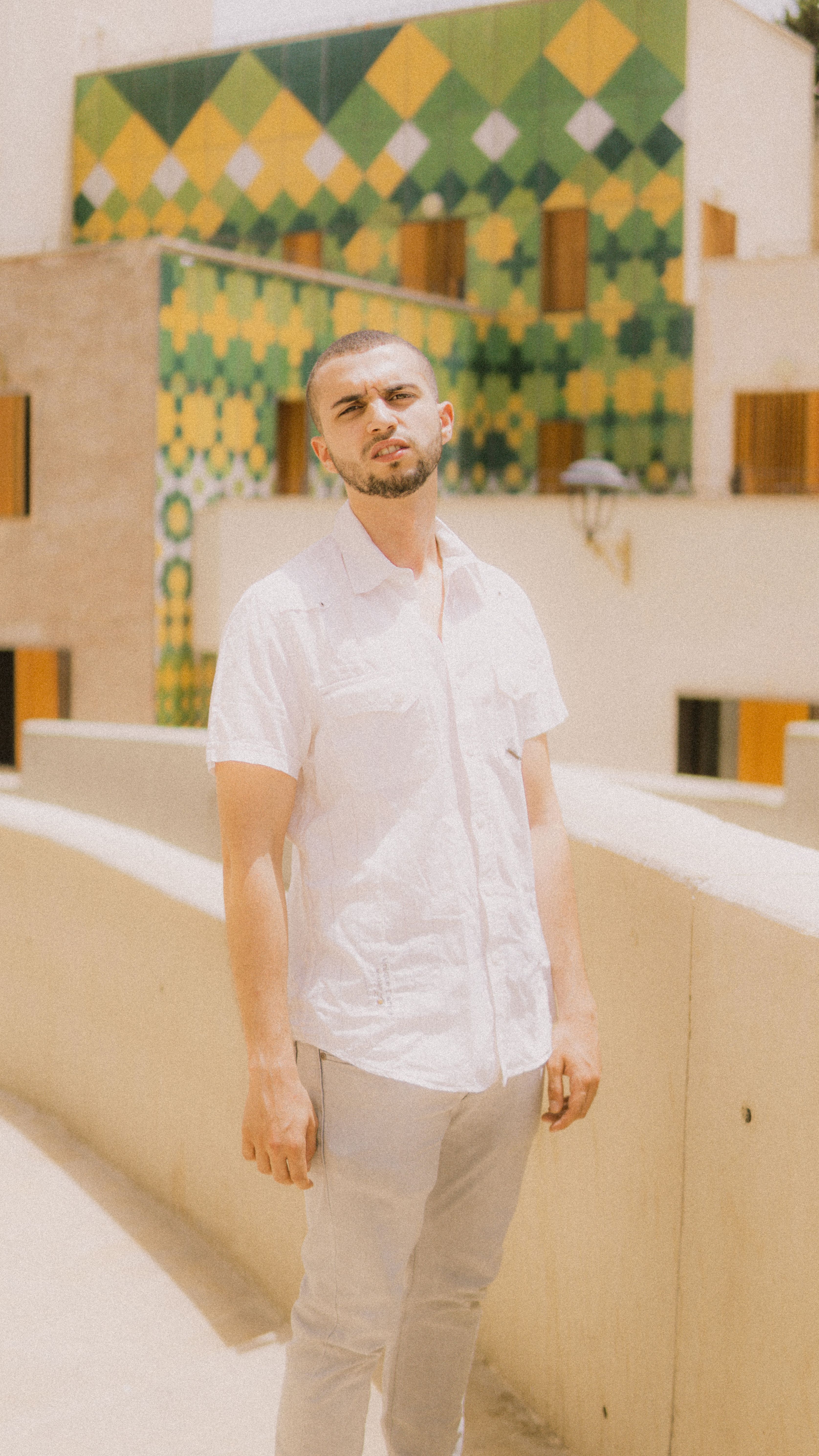 A fashionable man poses in the vibrant streets of Fes, Morocco, showcasing modern street style against patterned architecture.