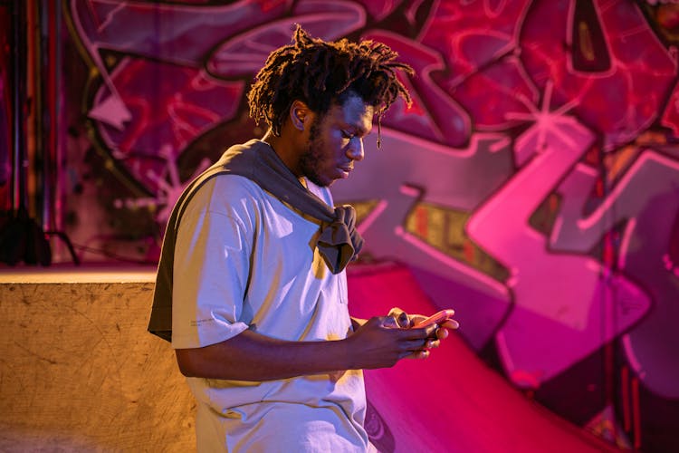 Young Man Using His Phone In A Skatepark 