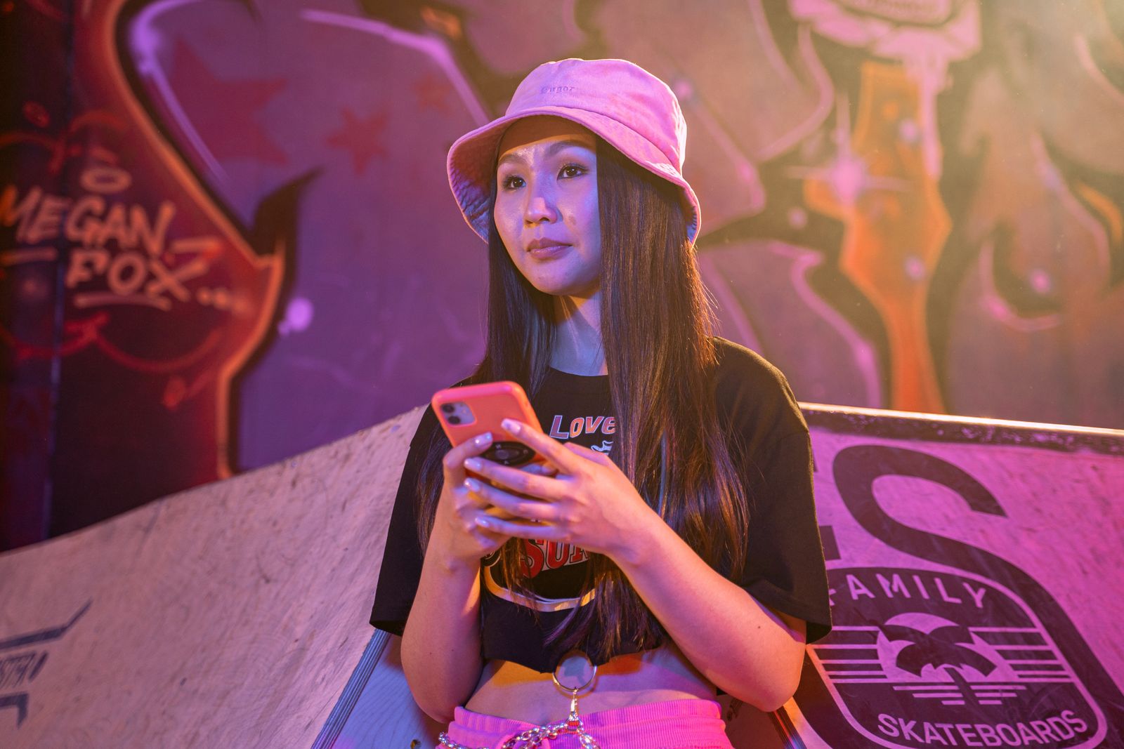 Young woman in a bucket hat and crop top using a mobile phone beside colourful graffiti