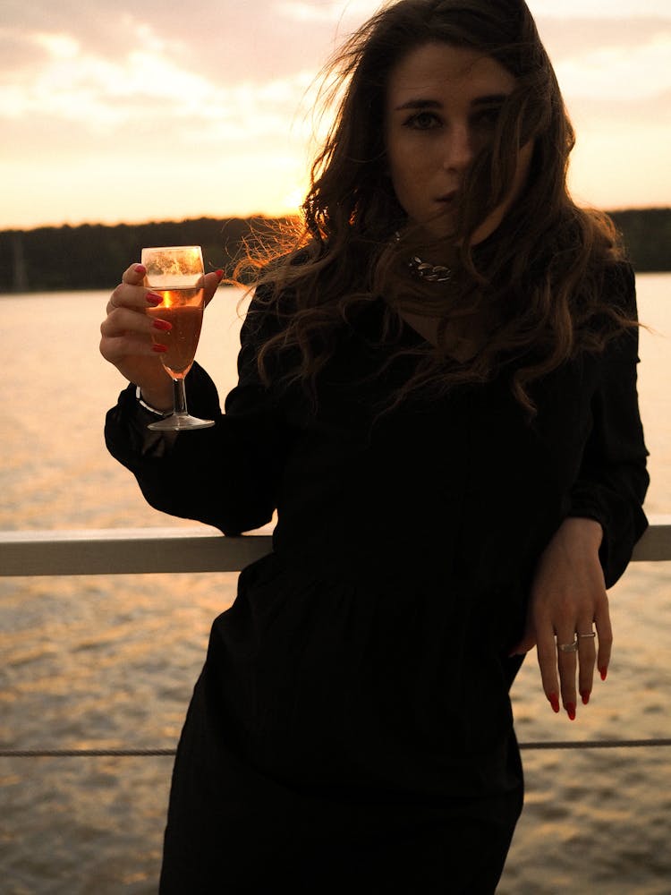 Woman In Black Outfit Holding A Glass Of Beer Near Body Of Water