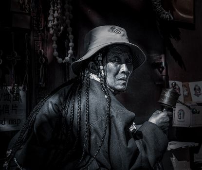 Elderly woman holding a prayer wheel, captured in black and white.
