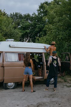 Young adults having fun with a vintage camper van during a road trip in nature.