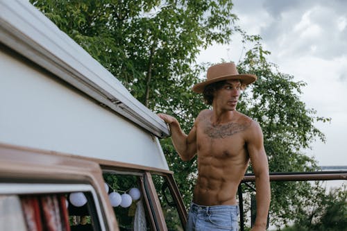 A Shirtless Man Standing by a Campervan