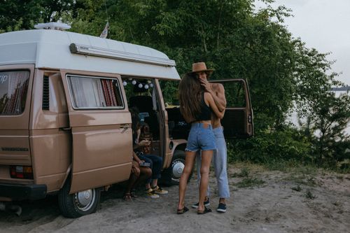 Free A young couple sharing a romantic moment by a vintage camper van in a scenic outdoor setting. Stock Photo