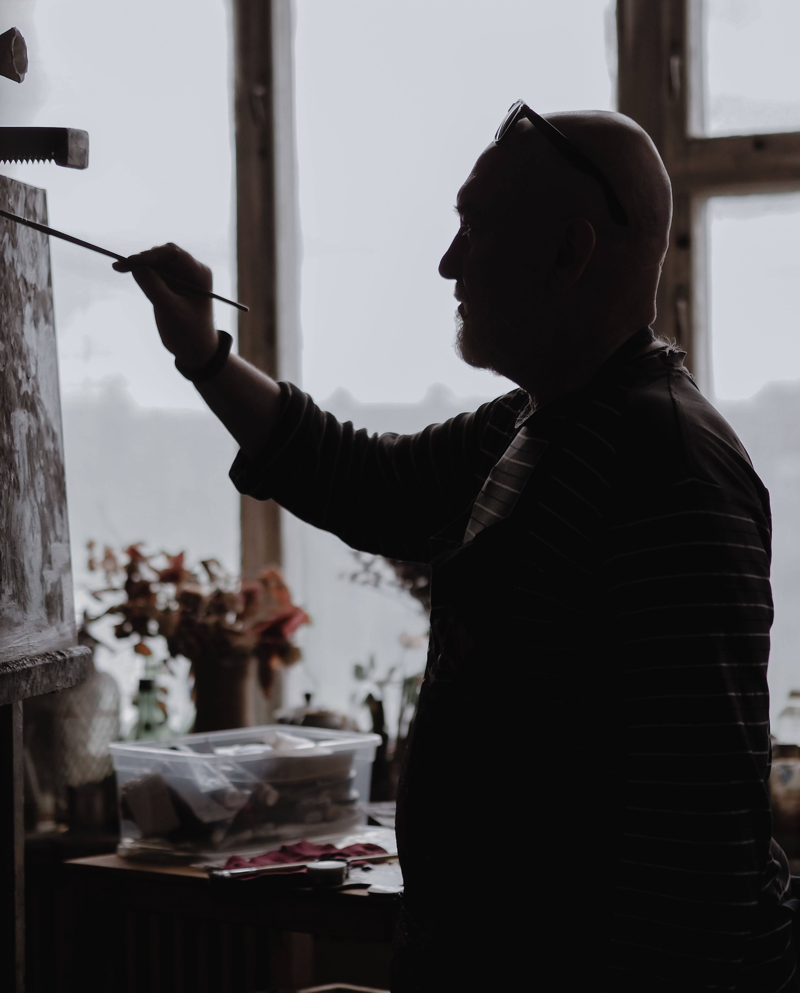 A silhouette of a male artist painting on canvas in a dimly lit studio.