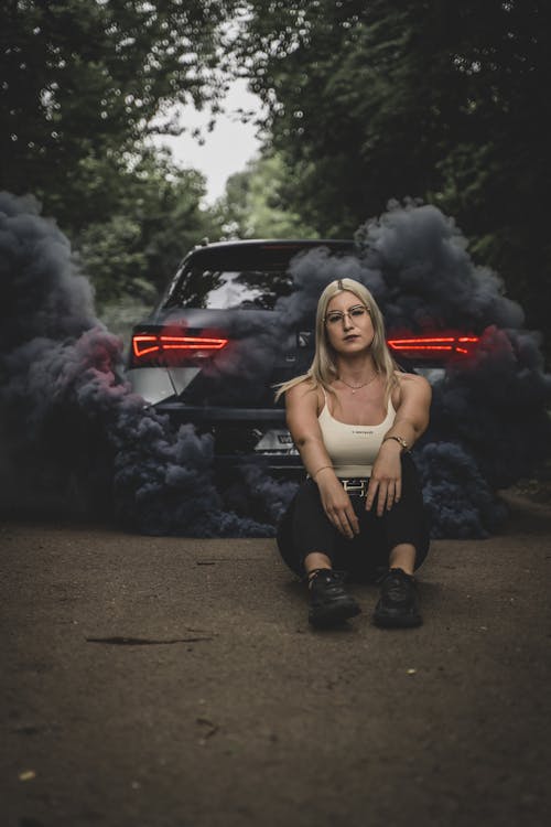 A Car with Black Fumes Coming out and a Woman Sitting on the Ground 