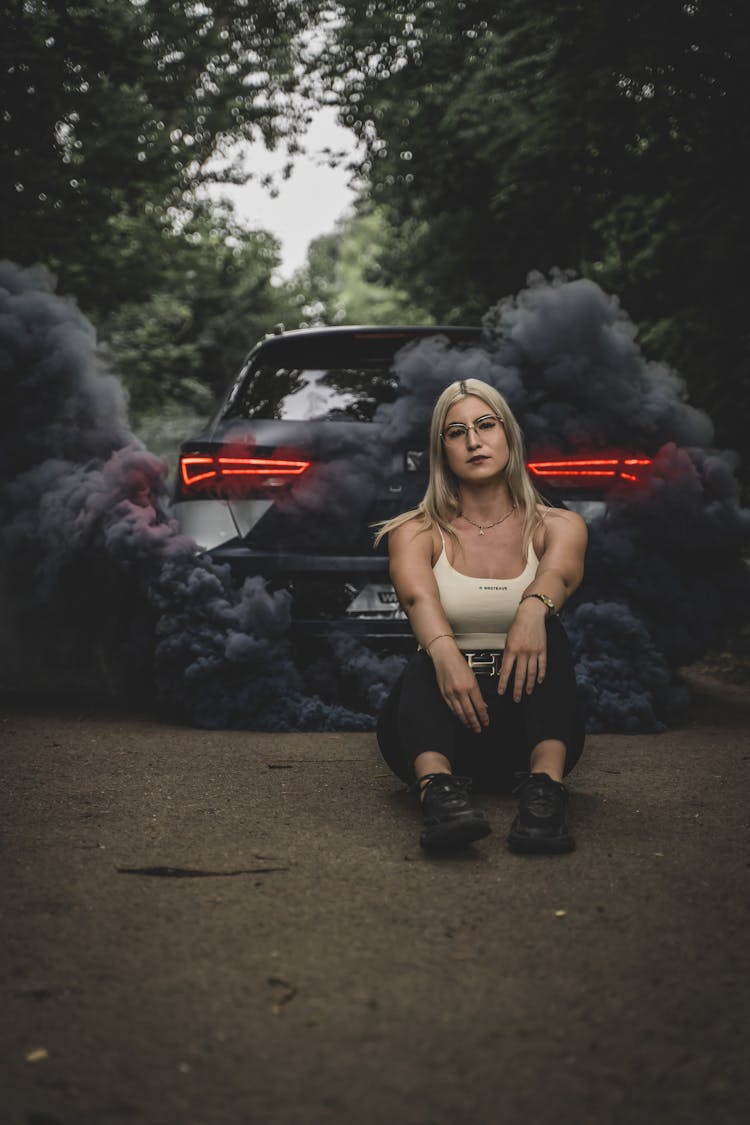 A Car With Black Fumes Coming Out And A Woman Sitting On The Ground 