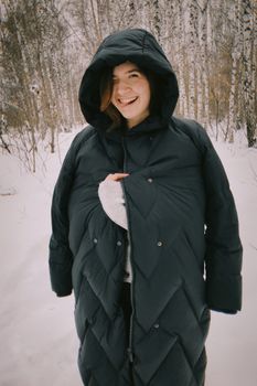 Young woman in a puffer coat smiling in a snowy forest setting, enjoying winter in Russia.